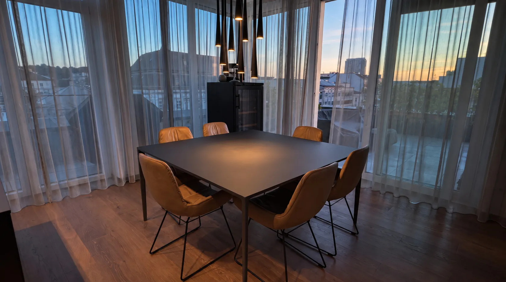 Essplatz im Penthouse in Wels am Abend, über dem Tisch eine Gruppe schlanker Hängeleuchten